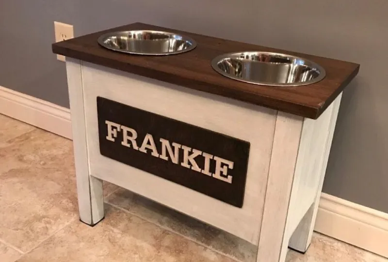 Tall white distressed dog bowl stand with a dark wood top and a dark nameplate reading Frankie in white letters, set against a grey wall